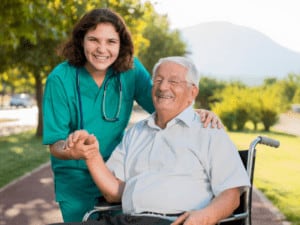 older man in wheelchair holds hands with homecare giver and that look happy