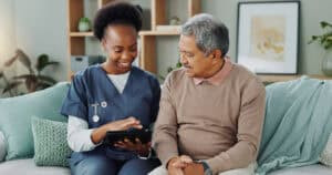 Home health care in Pittsburgh: Nurse shows senior patient information on a tablet at home.