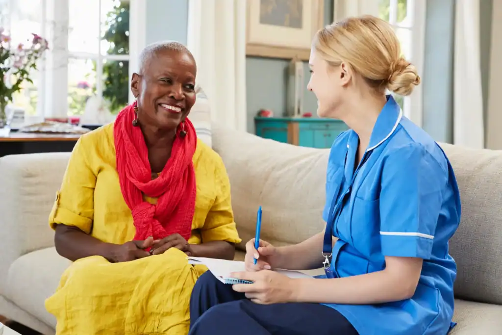 Smiling elderly woman talking to a home care nurse taking notes during a friendly visit