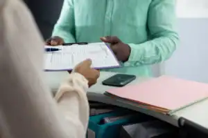 Medical receptionist handing patient a Medicaid waiver application form at the front desk.