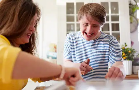 Two smiling adults with Down syndrome baking in a bright kitchen, possibly related to transfer home care.