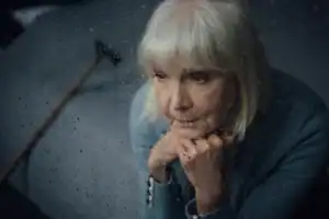 Elderly woman looking sad through a rainy window, hinting at depression in older adults.